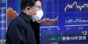 Bourse : un homme portant un masque passe devant un tableau électronique montrant des graphiques de récents mouvements de l'indice Nikkei
